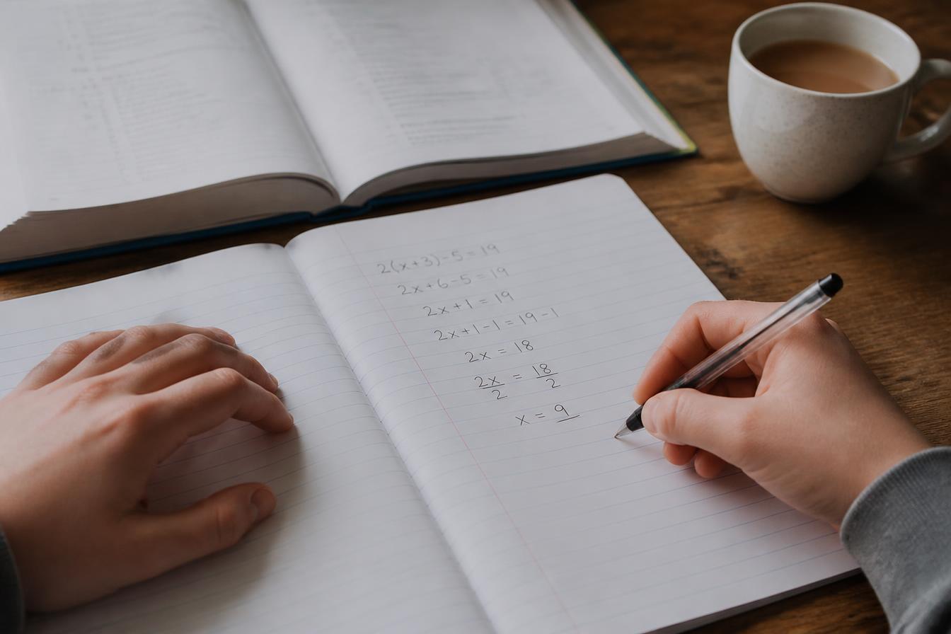 A hand working through an equation line by line in a notebook